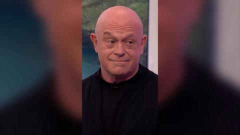 Ross Kemp is looking across to somebody off camera to the right of the screen and is wearing a black shirt