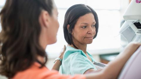 A woman goes for a mammogram.  She is pictured alongside a female medical professional. 