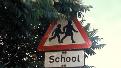 A traffic sign with two children crossing and the word "School".