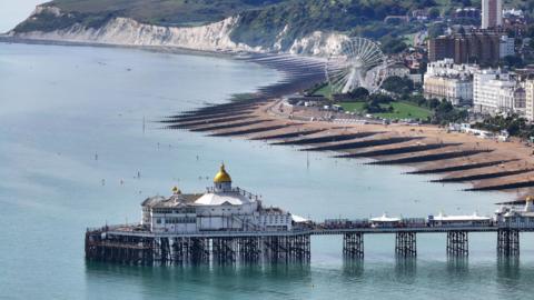 A 19th-century seaside pier in England. Cliffs and a big wheel can be seen on land in the background.