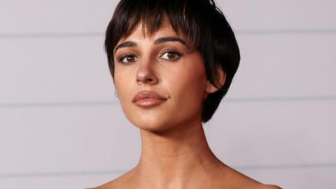 Naomi Scott looks at the camera. She has short dark hair, brown eyes and wears neutral makeup.