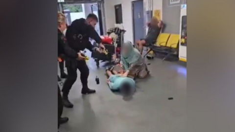 A police officer with his taser drawn stands over a man on the ground at the airport