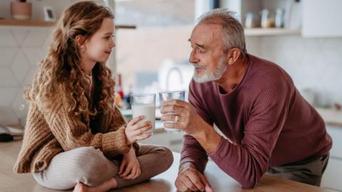 Senior man with his granddaughter toasting with glass of milk. - stock photo
