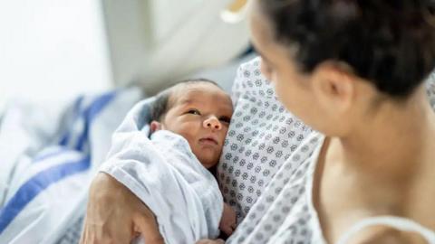 A mother holding and looking at her new baby in hospital clothing. 
