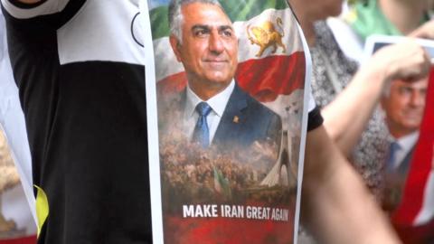 Man holds aloft a poster with and image of Reza Pahlavi and the words 'Make Iran Great Again'