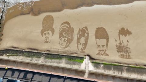 An aerial view of a sandy beach with drawings of Winston Churchill, Princess Diana, John Lennon, David Beckham and a steam train