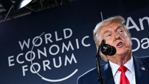 Close up shot of Donald Trump speaking into a microphone in front of a board with the words "World Economic Forum" on it.