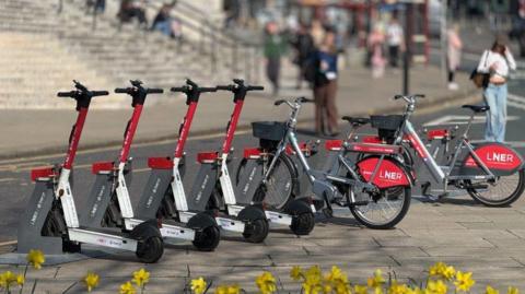 A row of parked e-scooters with red LNER branding in Leeds city centre. 