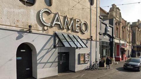 Outside Cameo nightclub in Eastbourne. Its name hangs in lights above a black front door and it is situated on a row of bars and shops.   