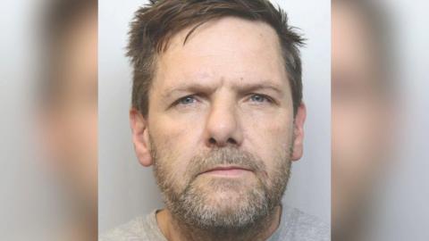 A police mugshot of Gavin Hope. He has brown spiky hair and a greying beard.