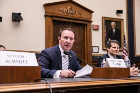 Man holds piece of paper in front of microphone at congressional hearing