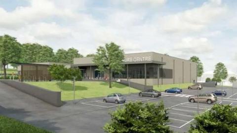 An artist's impression of a leisure centre building. The grey square building is shown sitting in a site surrounded by grass verges, trees and a car park.