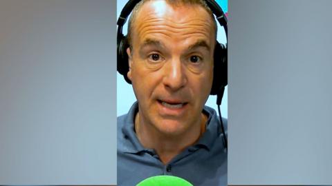 A man, Martin Lewis, wearing headphones, looking at the camera, with a green mic in front.