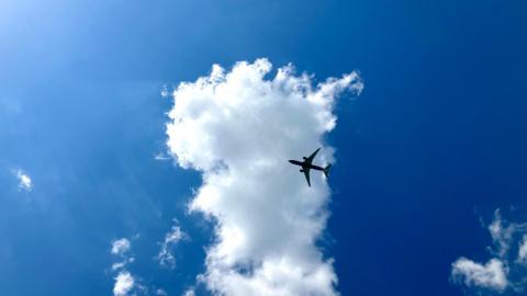 A jet plane with two engines flies in front of a white cloud with a blue sky in the background