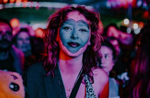 A woman with her face painted including the shape of a giant heart looks at the camera during a set at the Shindig Festival in Wiltshire