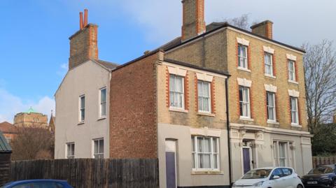 A three-storey brick building with several cars parked outside. 