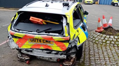 A car has gone into the back of a police vehicle leaving a huge dent in it. The body of the car is crushed inward and the rear windows have all been smashed. 