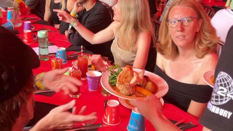 Woman sitting at a table looking up at a plate of roast food being handed to her