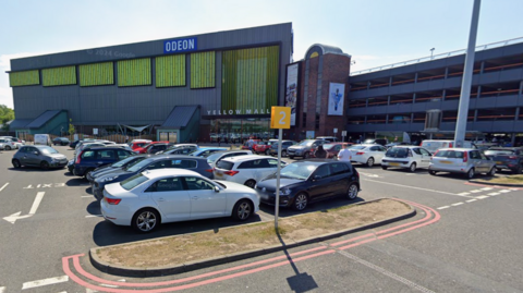 Cars parked in a car park. A building is behind it with the words Odeon and yellow mall. A car park building is to the right.