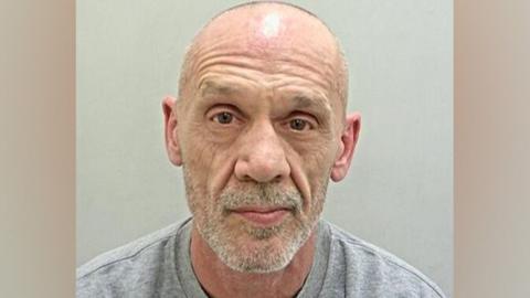 David Mitchell's police mugshot. He is bald, has white stubble and is wearing a grey sweatshirt