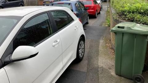A row of cars can been seen parked on the pavement. 