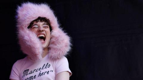Nemo, wearing a piunk fluffy hat and a t-shirt with the legend 'Marcello come here'
