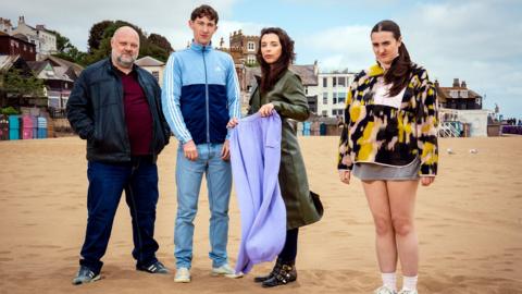 Four people on a beach looking at the camera