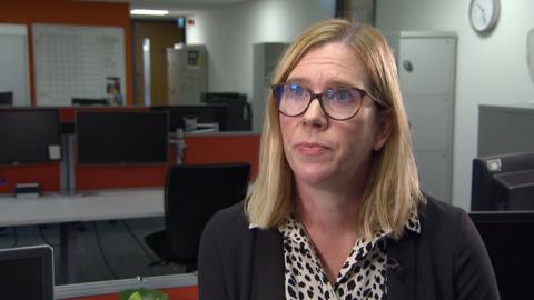 Detective Inspector Cheryl Lewendon is sitting in a police station office with a row of computers behind her