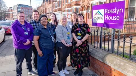 Seven people from Aspire pose outside its building on Thorne Road in Doncaster. The group are all smiling and wearing blue lanyards. A sign next to them reads: "Rosslyn House."