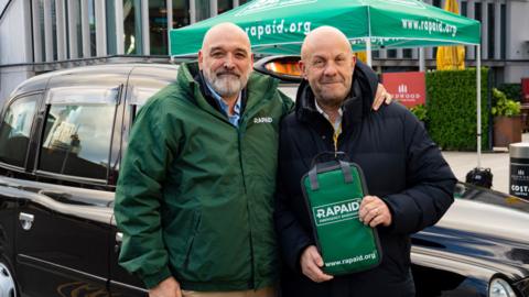 Alex Chivers posing with taxi driver, Howard Taylor, as he presents him with the RAPAID kit.