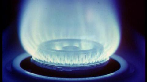 A gas burner is on and blue flames are coming out. It is a close up image and it the area around the burner is in darkness.