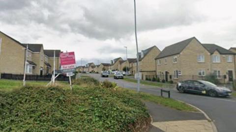A residential street with newly built houses, cars, 'for sale' signs and other street furniture.