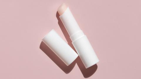 An open tube of lip balm against a pink background