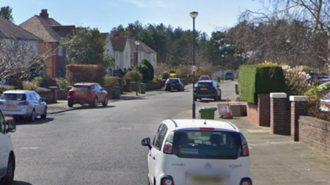 A street view of Lynton Road. There are cars lining the street and there and houses with red brick walls in front of their garden.