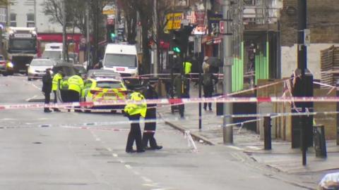 At least four Met Police officers are seen inside a police cordon on a high street.