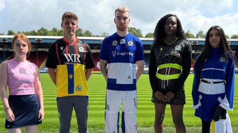Five models - three women and two men on Blackburn Rovers' pitch at Ewood Park wearing recycled football kits.