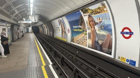 An empty platform at Oxford Circus with three people waiting for a Tube
