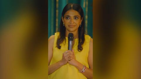 Sindhu Vee wearing a yellow top and holding a mic.