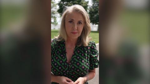Sarah looks into the camera as she stands in front of a grassy patch near White House
