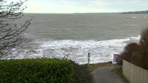 Photo of Helen's Bay beach from Saturday. The tied is in and there is no sand to be seen. The sky is grey and the water looks choppy. 