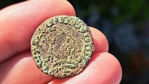 17th century coin on fingertips