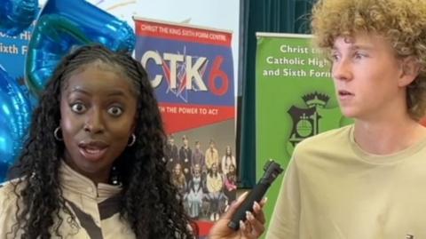 BBC presenter looking shocked and holding a microphone next to a boy.