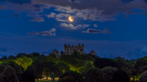 The blood moon above the top of Wollaton Hall which is poking up above the tree line.