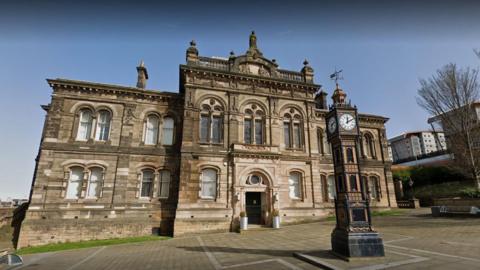 The front of Gateshead's Old Town Hall, a Grade II listed building in the town centre. A clock stands outside it.