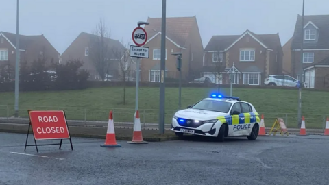 A road closure with police car parked near sign