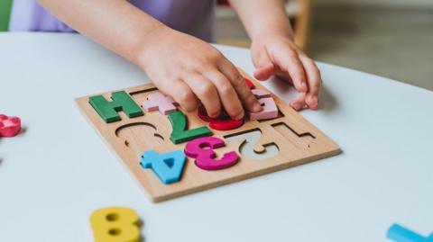 Close-up of little girl's hands playing with colorful numbers puzzle standing in the classroom in kindergarten