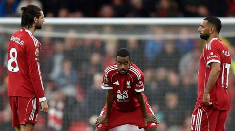 Three Liverpool players stand on the pitch looking dejected following their 2-1 defeat against Manchester United 