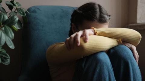 Stock image of an upset teenage girl covering her face with her hands.