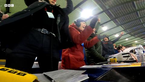 Dealbh a' sealltainn luchd-aithris BBC Radio nan Gàidheal a' dèanamh gàirdeachas aig Hampden