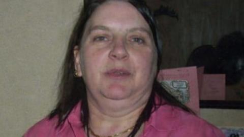 A woman with long brown hair wearing a pink shirt